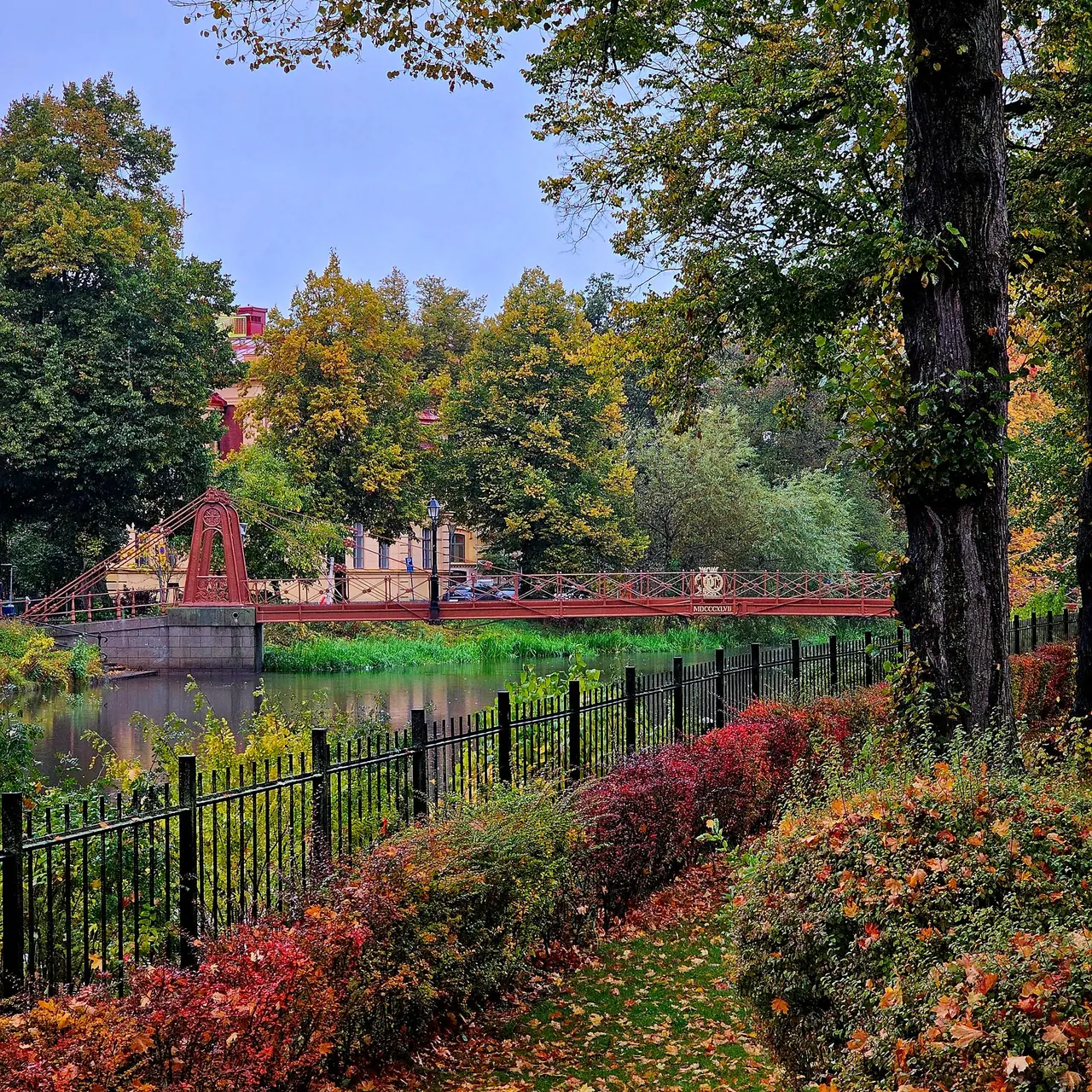 Autumn trees and red shrubs beside the Aura river in Turku, with a red footbridge