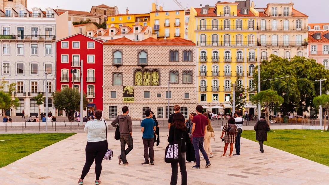 People crossing a Lisbon square lined with painted and tiled facades